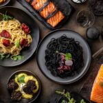 A table with black-themed foods like squid ink pasta, blackened salmon, and black forest cake.