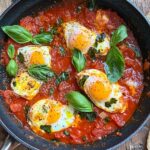 A skillet of Eggs in Purgatory with poached eggs in tomato sauce garnished with basil leaves.