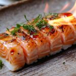 A flame-seared sushi dish garnished with fresh herbs on a ceramic plate.