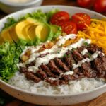 A colorful bowl of rice with beef, fresh vegetables, and dressing, presented on a rustic wooden table