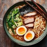 A bowl of ramen featuring soy-based broth, chashu pork, soft-boiled egg, nori, scallions, and noodles