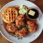 A plate of crispy fried chicken and golden waffles with maple syrup and butter